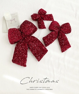 Close-up of three burgundy sequined Christmas bows on a soft white plush background