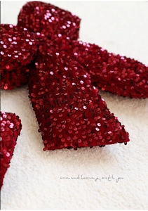 Macro shot of sequins on burgundy fabric bow ornament with plush white background