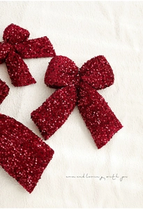 Close-up of burgundy sequined Christmas bows on a white plush texture background