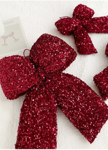 Detailed close-up of dark red sequin bows in three sizes on a soft white plush background