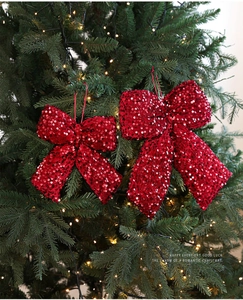Macro shot of two red sequined Christmas bow ornaments hanging on a green festive tree