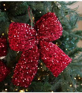 Close-up of burgundy sequined Christmas bow hanging on green pine with warm bokeh lights