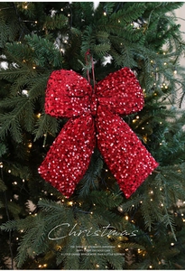 Macro shot of a red sequined Christmas bow hanging on a festive tree with warm lights