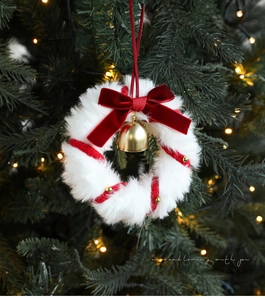 Detail of white plush Christmas wreath with red velvet bow, gold bells and ribbons