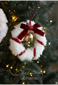 Detail of plush white Christmas wreath with red velvet bow and golden bell on a tree