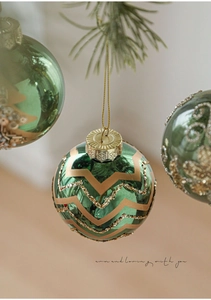 Close-up of dark green glass Christmas ball with golden glitter zigzag patterns on pine branch