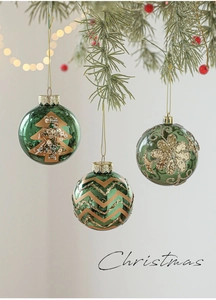 Detailed view of emerald green Christmas ornaments with gold glitter tree and floral patterns
