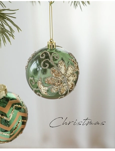 Close-up of green glass Christmas ornaments with gold glitter patterns on pine branches