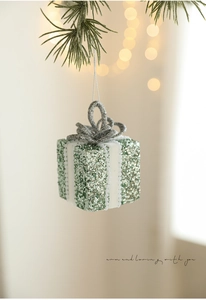 Macro shot of green glitter gift box ornament with white beaded ribbon on Christmas tree