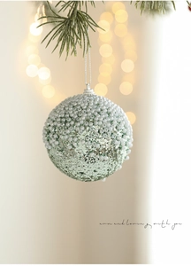 Close-up of green sequined Christmas ball with white beads on a pine tree branch