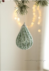 Detail of green teardrop Christmas ball with glitter and white beads on pine branch