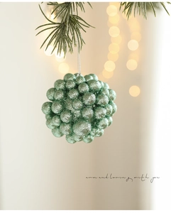Close-up of mint green glitter ball ornament hanging on a pine tree with warm bokeh light