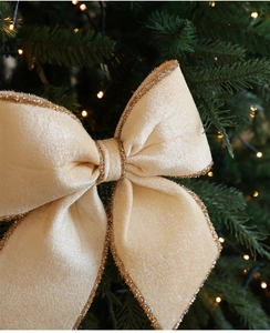 Dettaglio del fiocco di Natale in velluto champagne con bordi dorati su un ramo di pino