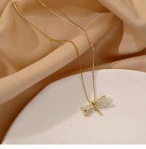 Close-up of golden dragonfly necklace with pavé crystal wings on elegant satin