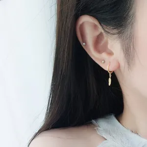 Detailed close-up of golden feather leaf earrings with minimalist silver ball studs
