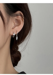 Detail of silver heart pavé and feather pendant earrings on model with soft lighting