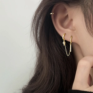 Close-up of gold chain earrings for double piercings with a zircon cross and ear cuff