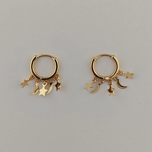 Detail of gold hoop earrings with star and moon tassels on a minimalist gray background