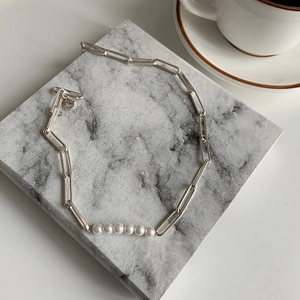 Silver paperclip chain necklace with five central white pearls on marble surface