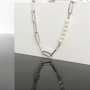Detail of elegant pearl necklace with silver paperclip chain links on a black background