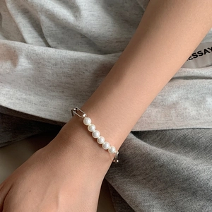 Elegant pearl and silver geometric chain bracelet worn on wrist over a grey background