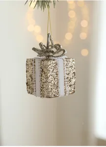 Golden glitter gift box ornament with white pearl ribbon hanging on a Christmas tree