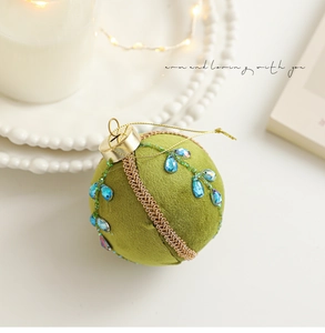 Détail de la boule de Noël en velours vert avec gemmes bleues et rubans tressés dorés