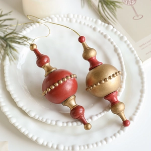 Vintage red and gold spindle-shaped wooden Christmas ornaments on white ceramic plates