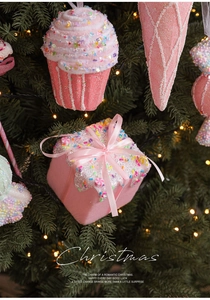 Pink cupcake, gift box and cone ornaments hanging on a lighted Christmas tree