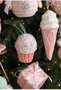 Close-up of pink macaron cupcakes and ice cream ornaments on a lit Christmas tree