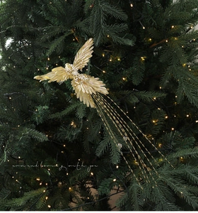 Close-up of a golden bird ornament with pearls and glitter on a green Christmas tree