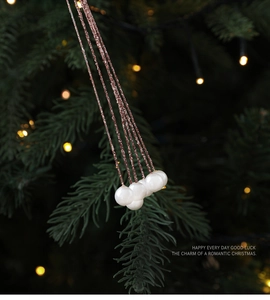 Close-up of pearl Christmas ornaments with rose gold glitter hanging on a lit Xmas tree
