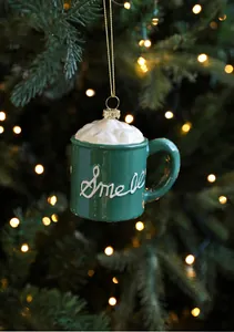 Detail of a green mug Christmas ornament with cream top on a festive tree branch