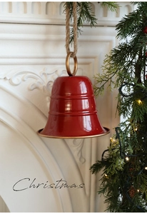 Dettaglio campana di Natale in metallo rosso con anello dorato e corda sul camino