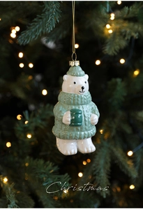 Detail of polar bear Christmas ornament with green sweater on holiday tree branch