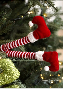 Jambes d'elfe dans un sapin de Noël avec tissu rayé et bottes en velours rouge peluche