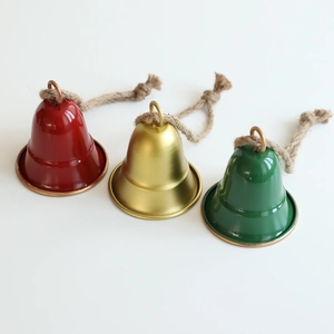 Tre campane di Natale in metallo rosso, oro e verde con corde di juta su fondo bianco