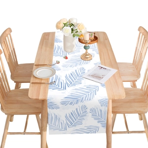 Linen table runner with blue palm leaf print on a wooden dining table setup