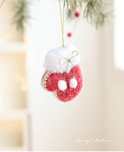 Detail of red felt Christmas glove ornament with white faux fur and gold bow on pine branch