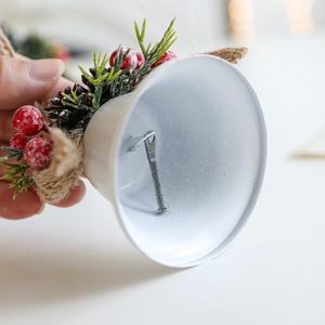 White metal Christmas bell ornament with pine needles, red berries and natural pine cones