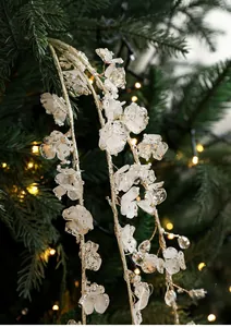 Close-up of white acrylic Christmas branch with gold glitter and warm bokeh lights