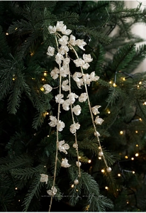 Close-up of white festive floral picks with gold glitter and pearls on a green Christmas tree