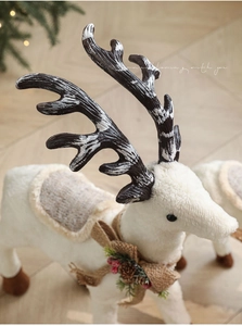Detail of a white plush Christmas reindeer with pine cones, red berries and burlap bow