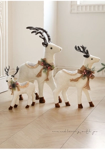 Close-up of three white plush reindeer figurines with pine cones and festive bows