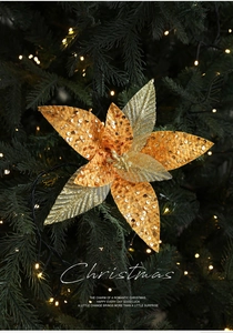 Close-up of golden orange sequined Christmas flower on decorated pine branch with lights