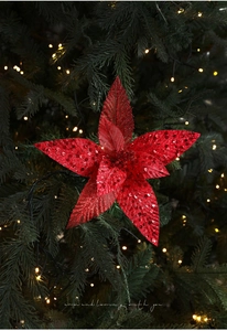Detail of red glitter poinsettia flower ornament hanging on a lush Christmas tree branch