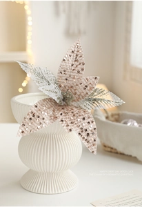 Detail of rose gold sequined Christmas poinsettia flower in a white ribbed ceramic vase