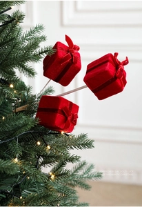 Detail of red flocked Christmas gift box pick with bow ornament on a festive tree
