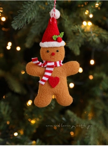 Plush gingerbread man ornament with red hat hanging on a festive Christmas tree with lights