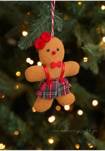 Detailed view of handmade felt gingerbread man ornament with red bow on a Christmas tree